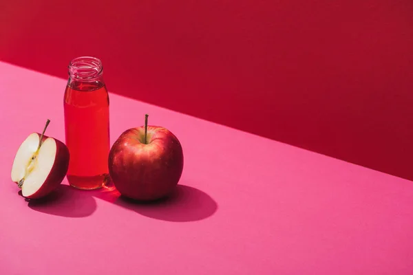 Fresh juice in bottle near apples on red and pink background — Stock Photo