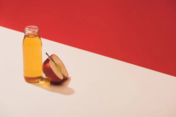 Frischer Saft in der Flasche in der Nähe der Apfelhälfte auf rotem Hintergrund — Stockfoto