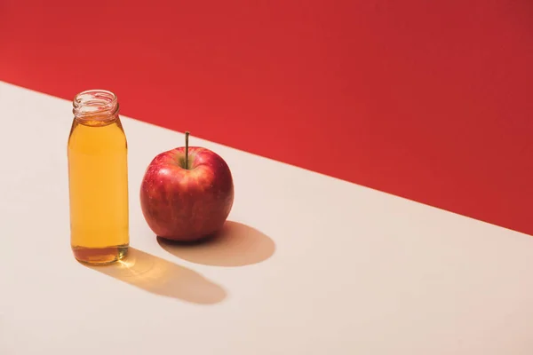 Suco fresco em garrafa perto de maçã no fundo vermelho — Fotografia de Stock