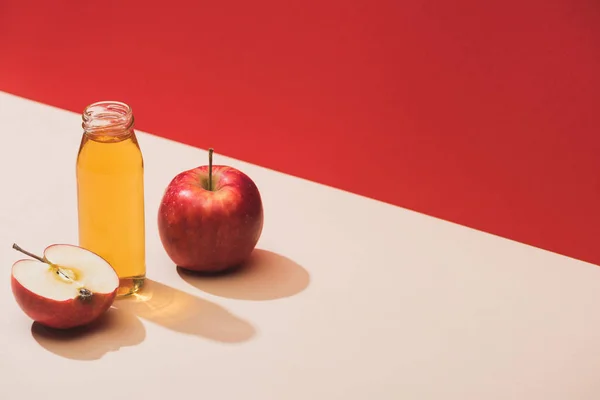Jus frais en bouteille près des pommes sur fond rouge — Photo de stock