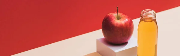 Suco fresco em garrafa perto de maçã e cubo branco no fundo vermelho, tiro panorâmico — Fotografia de Stock