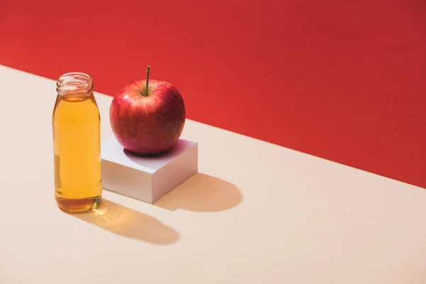 Zumo fresco en botella cerca de manzana y cubo blanco sobre fondo rojo - foto de stock