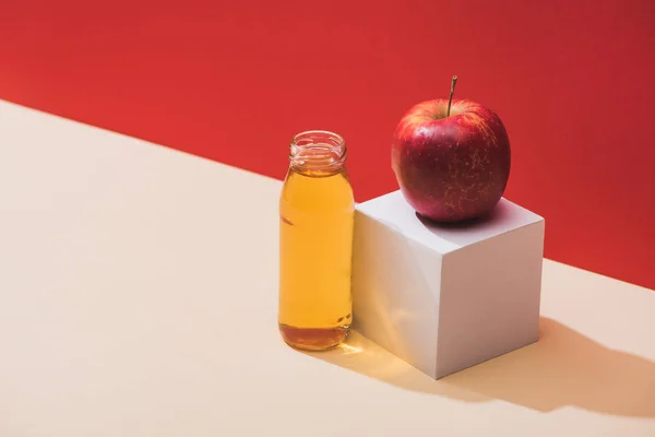 Zumo fresco en botella cerca de manzana y cubo blanco sobre fondo rojo — Stock Photo