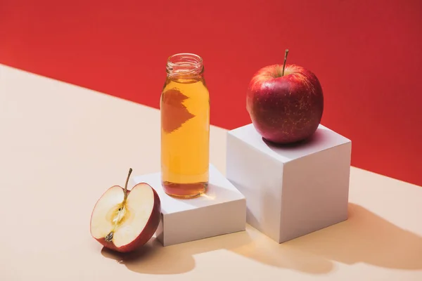 Zumo fresco en botella cerca de manzanas y cubos blancos sobre fondo rojo - foto de stock