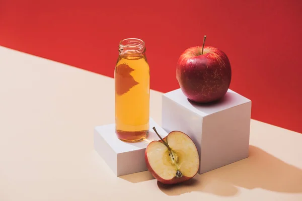 Zumo fresco en botella cerca de manzanas y cubos blancos sobre fondo rojo — Stock Photo
