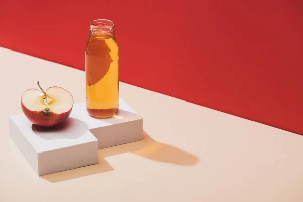 Fresh juice in bottle near apple half and white cubes on red background — Stock Photo