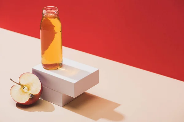 Frischer Saft in der Flasche in der Nähe der Apfelhälfte und weiße Würfel auf rotem Hintergrund — Stockfoto