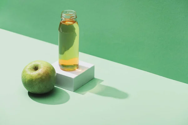 Frischer Saft in der Nähe von Apfel und weißem Würfel auf grünem und türkisfarbenem Hintergrund — Stockfoto