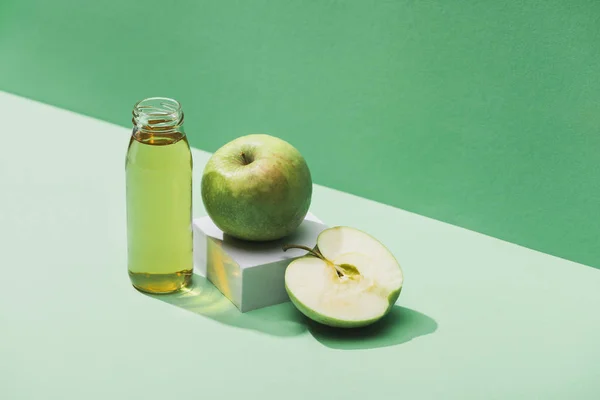 Fresh juice near apples and and white cube on green and turquoise background — Stock Photo