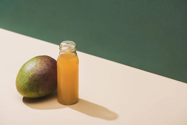 Fresh juice in bottle near mango on green background — Stock Photo