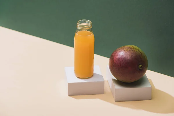 Свежий сок в бутылке рядом с манго и белые кубики на зеленом фоне — стоковое фото