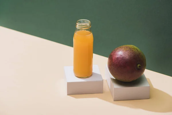 Frischer Saft in Flasche in der Nähe von Mango und weißen Würfeln auf grünem Hintergrund — Stockfoto