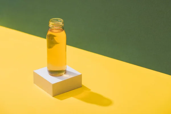Fresh juice in bottle on white cube on green and yellow background — Stock Photo