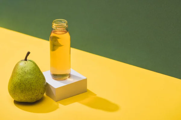 Succo fresco in bottiglia vicino alla pera e cubo bianco su sfondo verde e giallo — Foto stock