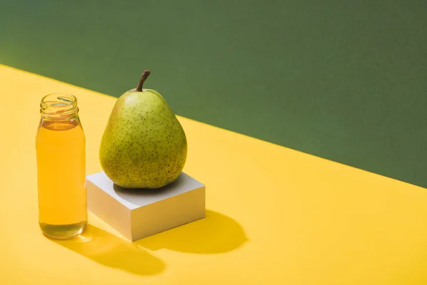 Zumo fresco en botella cerca de pera y cubo blanco sobre fondo verde y amarillo - foto de stock