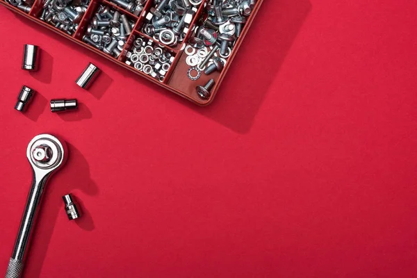 Top view of wrench with nozzles and tool box with bolts and nuts on red background — Stock Photo