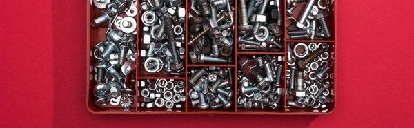 Top view of metal wood screws and nuts in tool box on red background, panoramic shot — Stock Photo