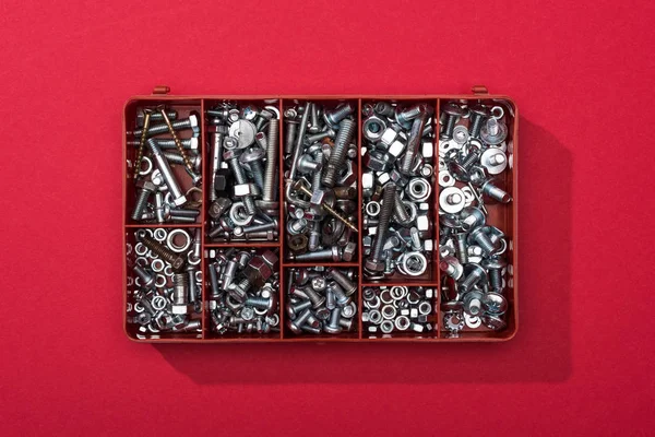 Vista dall'alto di dadi in metallo e viti in legno in cassetta degli attrezzi su sfondo rosso — Foto stock
