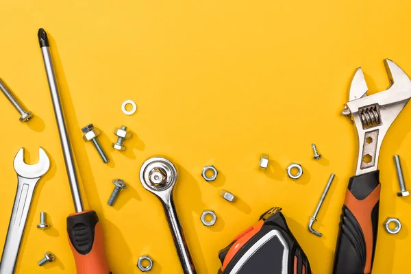 Vista superior del conjunto de herramientas con tuercas y pernos sobre fondo amarillo - foto de stock