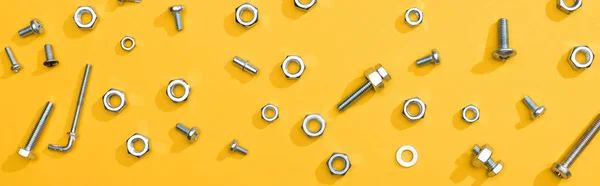 Top view of metal nuts and bolts on yellow background, panoramic shot — Stock Photo