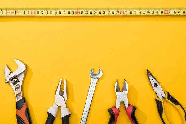 Top view of industrial measuring tape near wrenches and pliers on yellow background — Stock Photo
