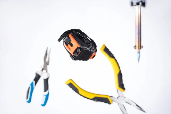Selective focus of measuring tape with pliers and soldering iron levitating in air isolated on white — Stock Photo