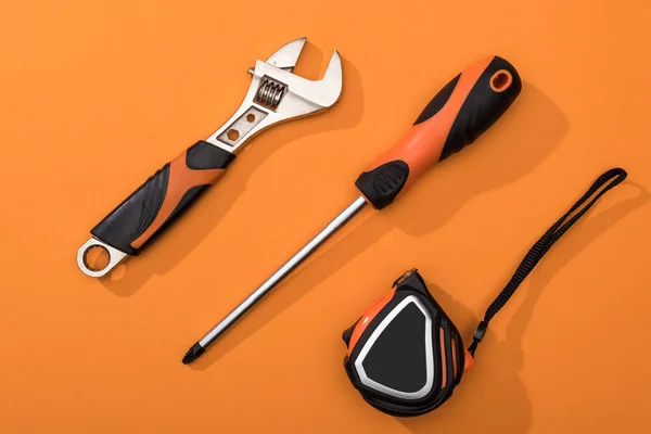 Top view of wrench, screwdriver and measuring tape on orange background — Stock Photo