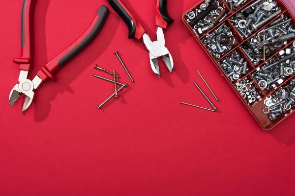 Vue du dessus de la boîte à outils avec pinces et clous sur la surface rouge — Photo de stock