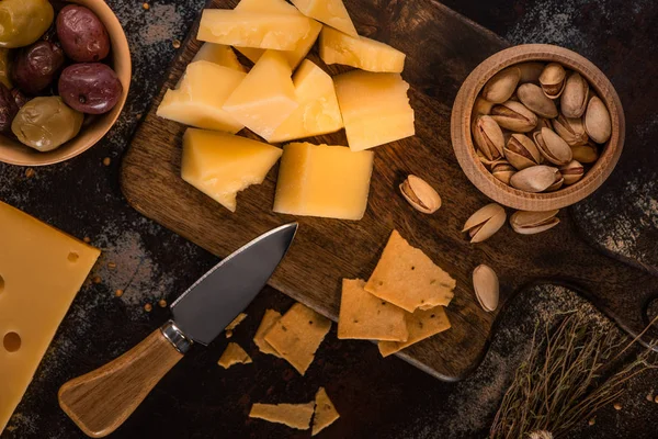 Вид зверху сирної тарілки з фісташками, оливками та крекерами на дерев'яній обробній дошці біля ножа — стокове фото