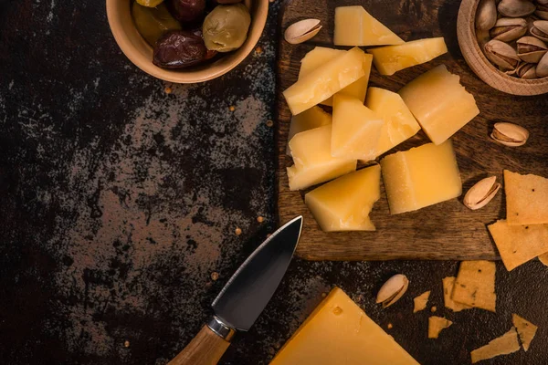 Top view of cheese platter with pistachios, olives and crackers on wooden cutting board near knife — Stock Photo