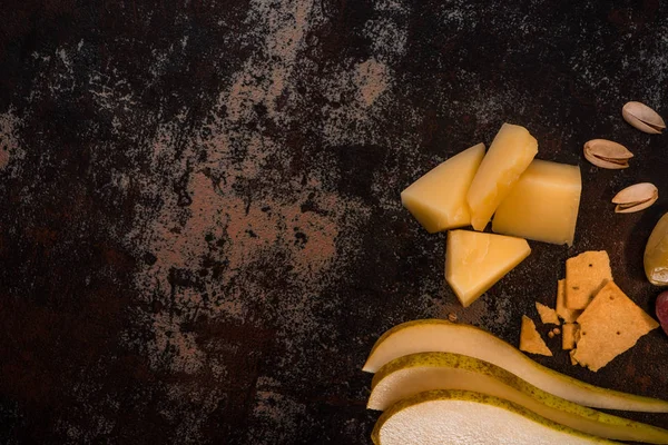 Top view of cheese with pistachios, sliced pear, olives and crackers on weathered surface — Stock Photo