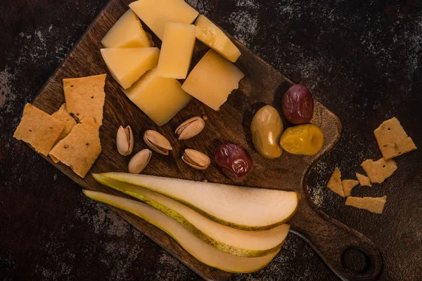 Top view of cheese platter with pistachios, sliced pear, olives and crackers on weathered surface — Stock Photo