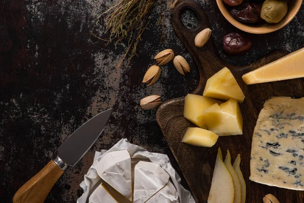 Vue de dessus de plateau de fromage avec pistaches, poire tranchée, olives et couteau sur la surface altérée — Photo de stock