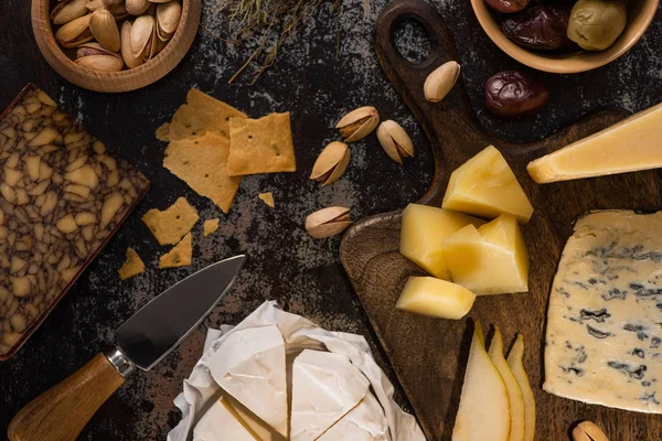 Top view of cheese platter with pistachios, sliced pear, olives and crackers on weathered surface — Stock Photo