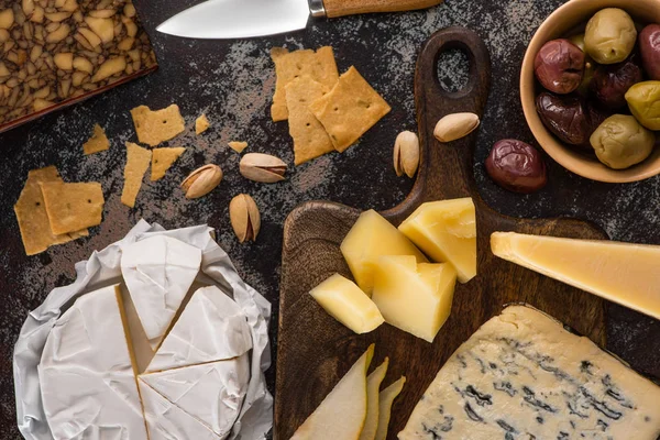 Top view of cheese platter with pistachios, sliced pear, olives and crackers on weathered surface — Stock Photo