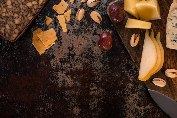 Vista superior de la bandeja de queso con pistachos, pera en rodajas, aceitunas y galletas saladas en la superficie erosionada - foto de stock