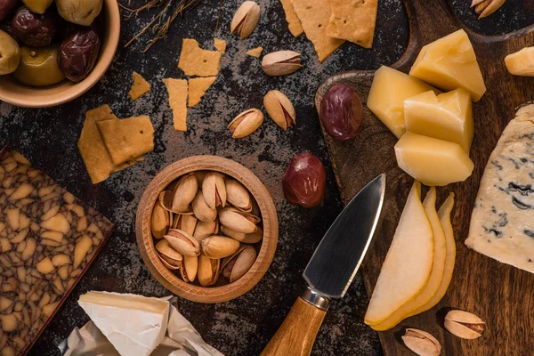 Top view of cheese platter with pistachios, sliced pear, olives and crackers on weathered surface — Stock Photo