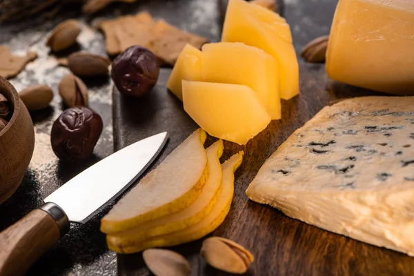 Close up view of cheese platter with knife, sliced pear, pistachios, olives and crackers — Stock Photo