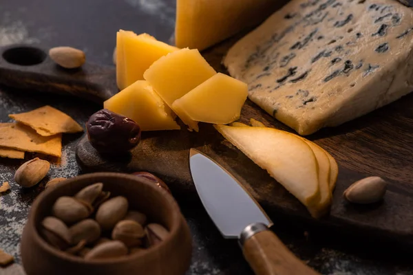 Vista de cerca de bandeja de queso con cuchillo, pera en rodajas, pistachos, aceitunas y galletas saladas - foto de stock