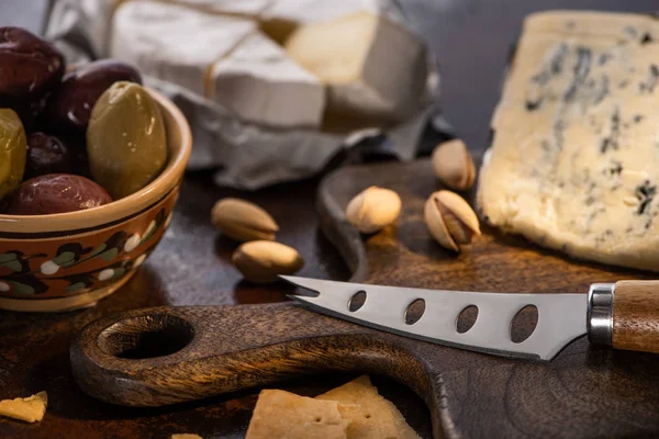 Selective focus of dorblu and brie cheese with olives and pistachios near knife — Stock Photo