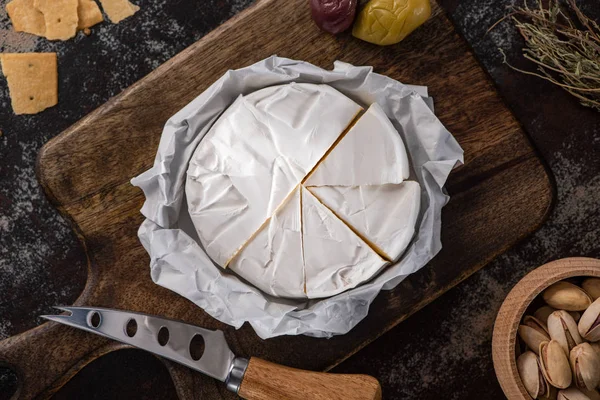 Vista superior del plato de queso brie con aceitunas, galletas saladas y pistachos cerca del cuchillo - foto de stock