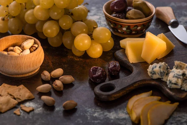 Cheese platter with olives, fruits, crackers and pistachios near knife — Stock Photo