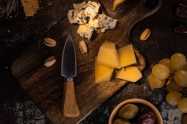 Вид зверху сирної тарілки з оливками, виноградом і фісташками біля ножа — стокове фото