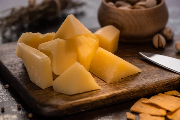 Закрыть вид на блюдо с сыром Grana Padano, кракерами и фисташками возле ножа — стоковое фото