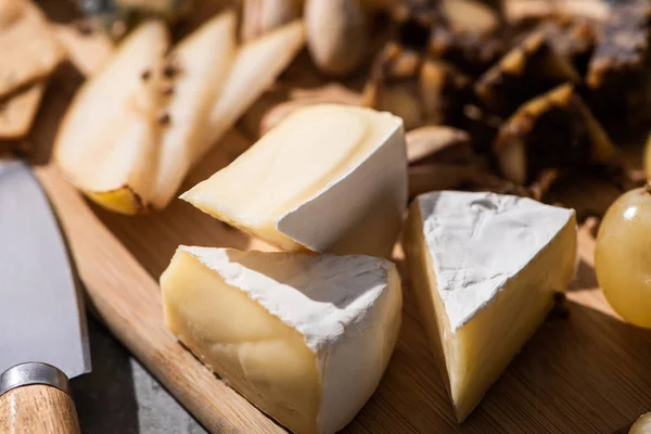 Selective focus of pieces of Camembert cheese with slices of pear and grape on cutting board next to knife — Stock Photo
