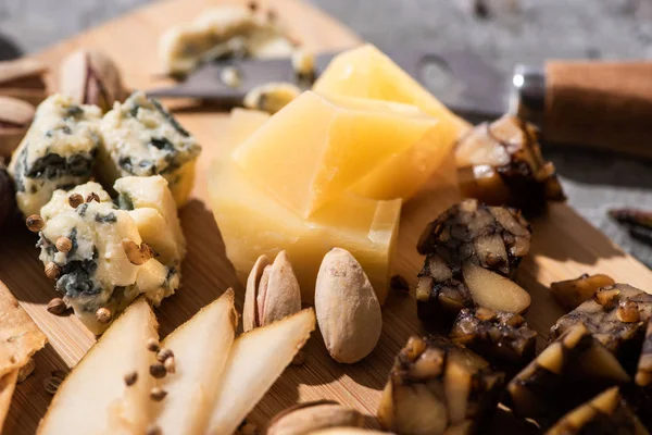 Enfoque selectivo de trozos de grana padano, dorblu y queso de nuez con pistachos, rodajas de pera y semillas en tabla de cortar - foto de stock