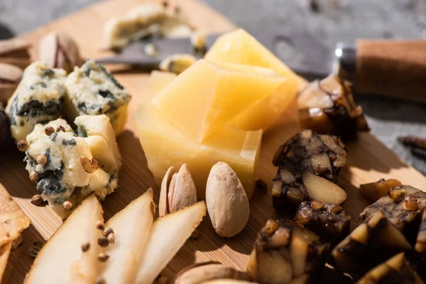 Selective focus of pieces of grana padano, dorblu and nut cheese with pistachios, slices of pear and seeds on cutting board — Stock Photo