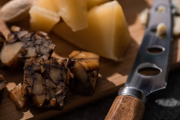 Enfoque selectivo de trozos de queso de nuez y grana padano junto a cuchillo en tabla de cortar - foto de stock