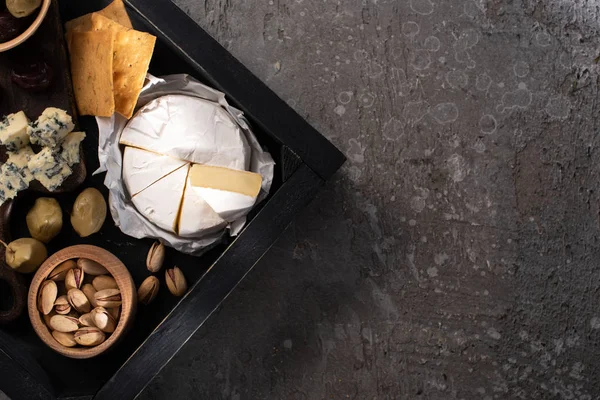 Top view of tray with pieces of camembert, dorblu, dried olives, crackers, pistachios on grey background — Stock Photo