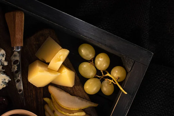 Vista superior da bandeja com faca suja ao lado de pedaços de queijo, fatias de pêra e uvas isoladas em preto — Fotografia de Stock